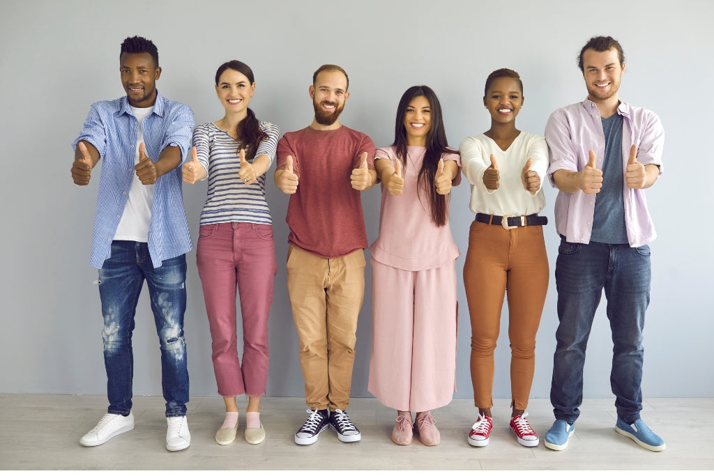 Group of six people standing together, giving thumbs up, against a plain background