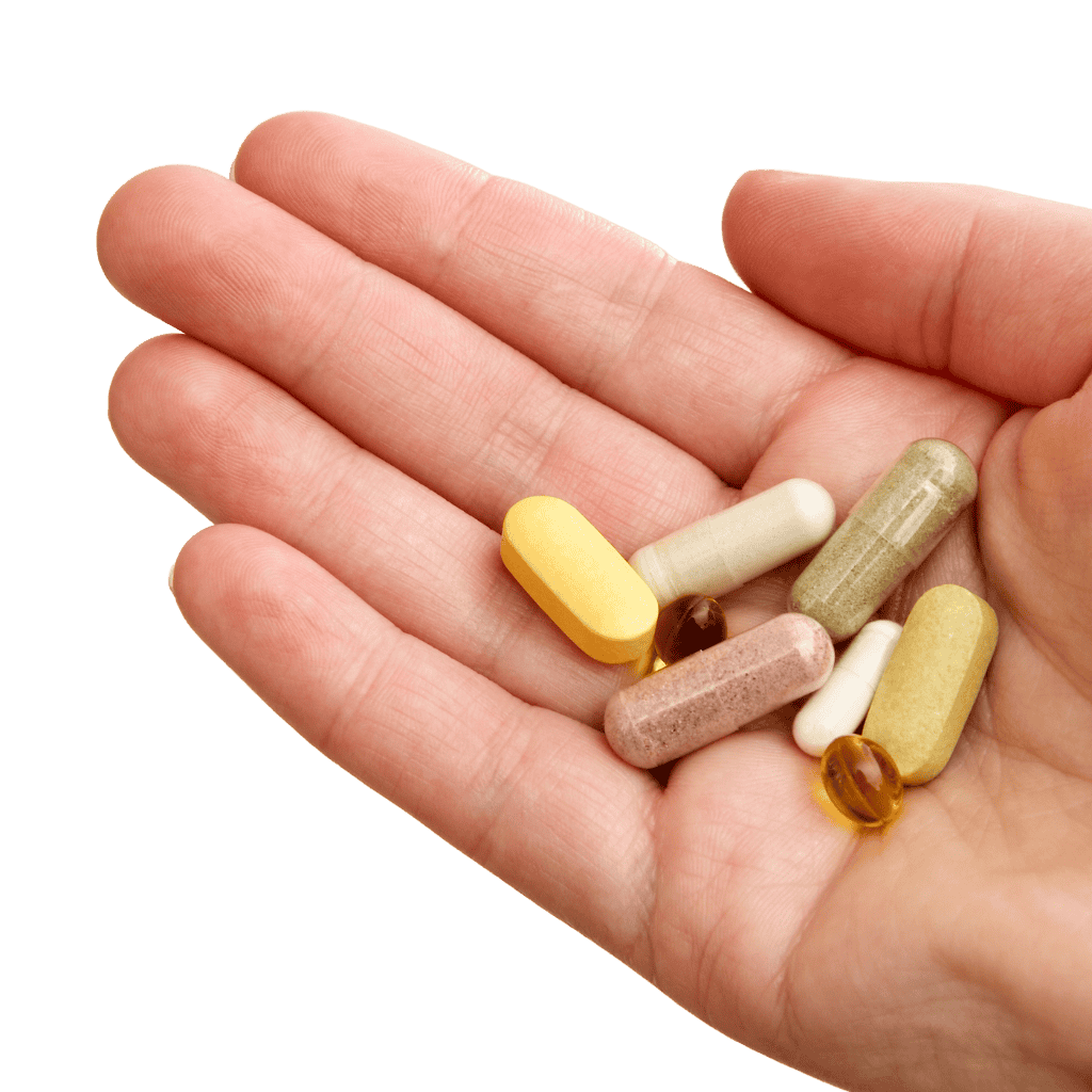 Hand holding various pills and capsules on a green background