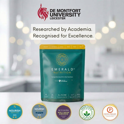 Emerald Nutrition supplement package with De Montfort University branding and certification logos on a blurred kitchen background.