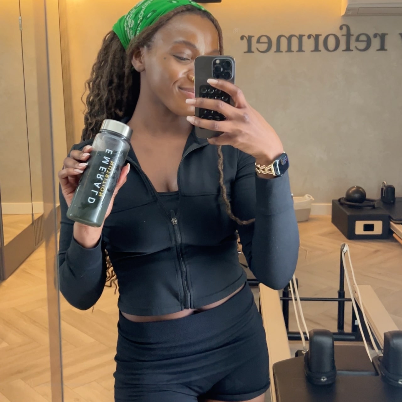 Woman in athletic wear taking a mirror selfie with a water bottle in a gym setting