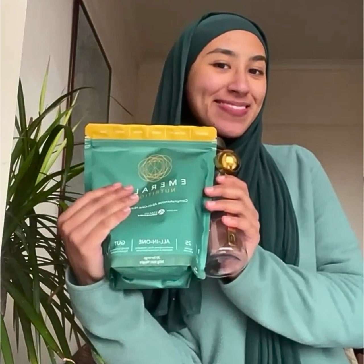 Woman holding a green coffee bag and a glass of water indoors