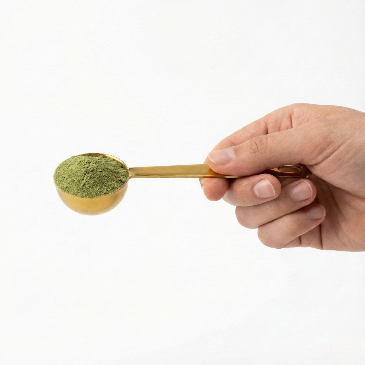 Hand holding a gold spoon filled with green powder against a white background