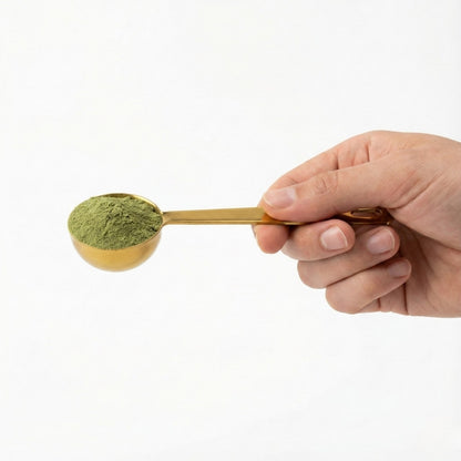Hand holding a gold spoon filled with green powder against a white background