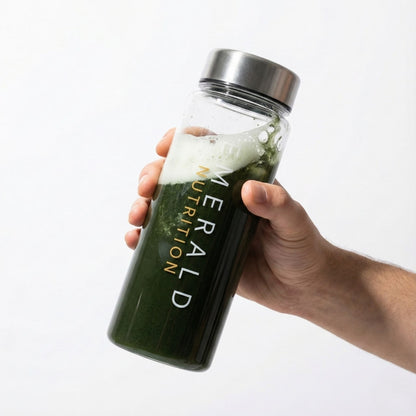 Hand holding a glass bottle with a green liquid labeled 'Emerald Nutrition' on a white background