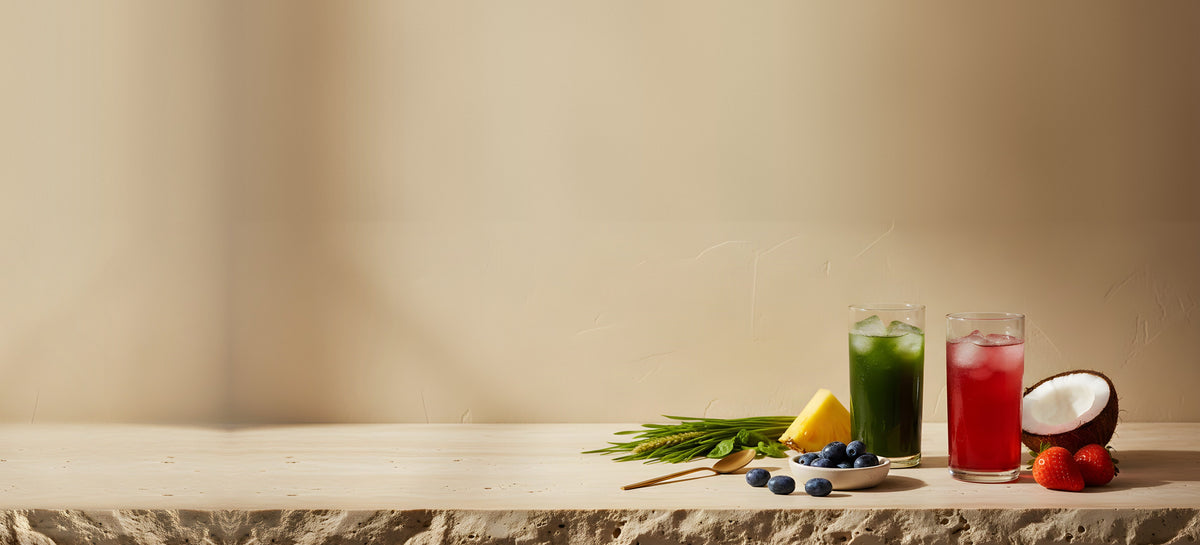 Emerald Nutrition Supergreens and Ignite iced drinks on rough-cut stone with fresh wheatgrass, pineapple, haskap berries, strawberries and coconut