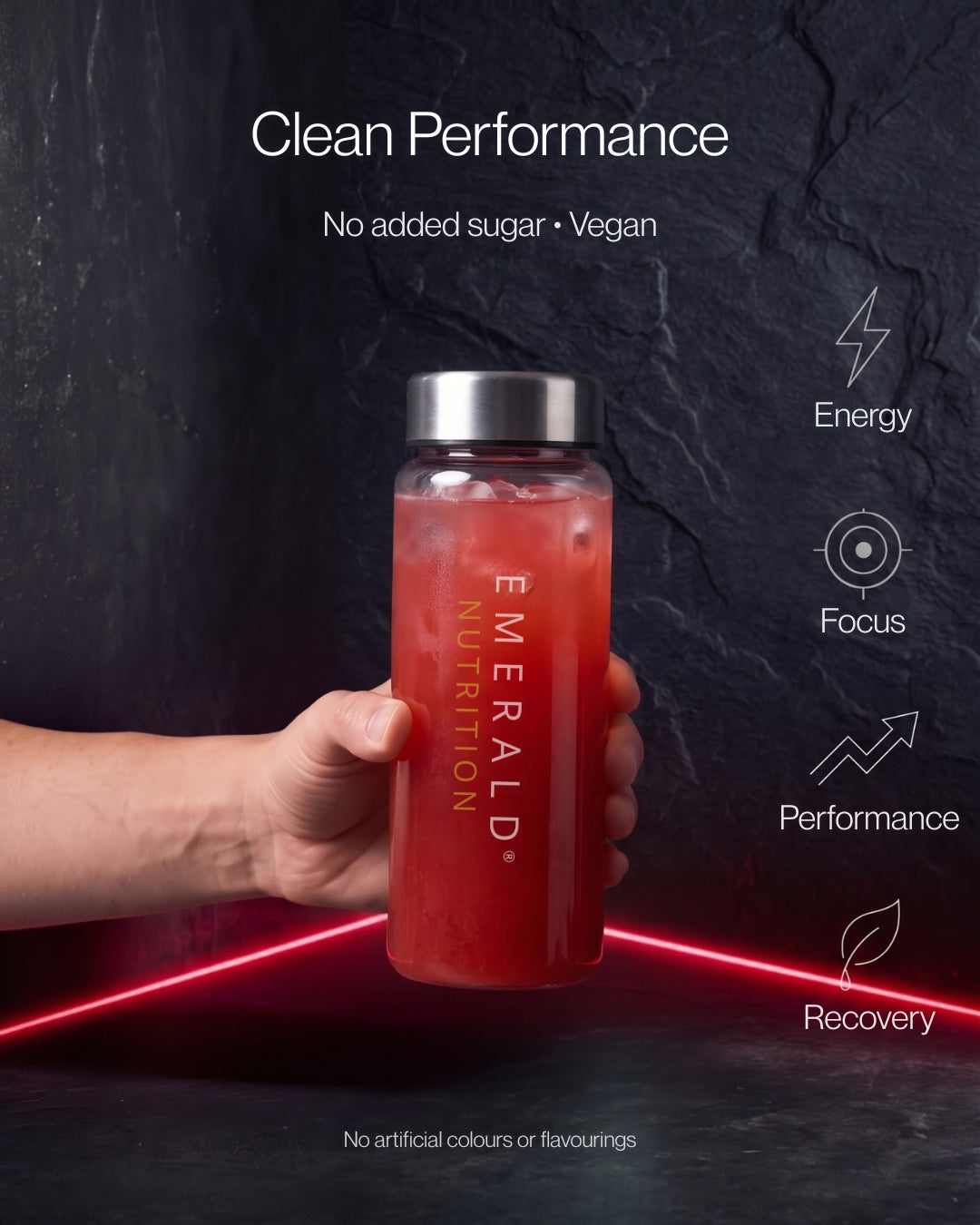 A hand holds a clear plastic water bottle filled with a red drink. The bottle has a silver cap and vertical 'EMERALD NUTRITION' branding.