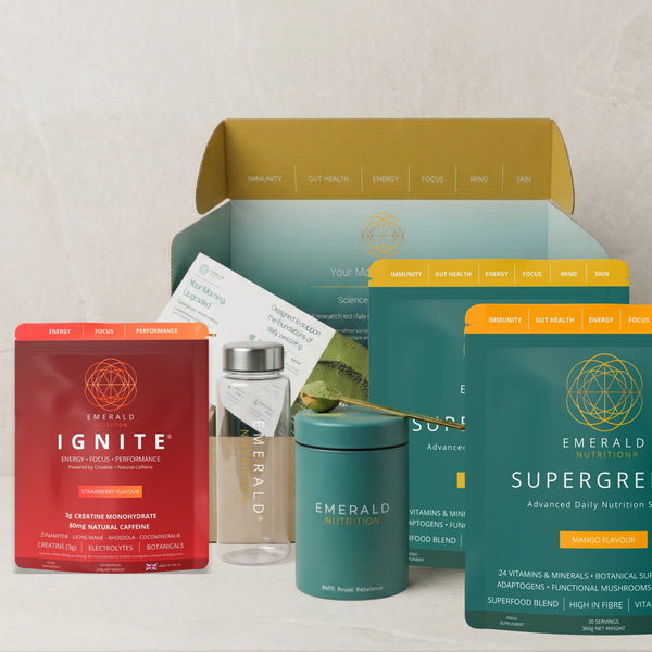 Emerald Nutrition wellness gift set featuring a red Ignite box, a teal Supergreen box, a teal container, a clear bottle with a silver cap, and an open gold-and-teal box in the background on a light marble surface.