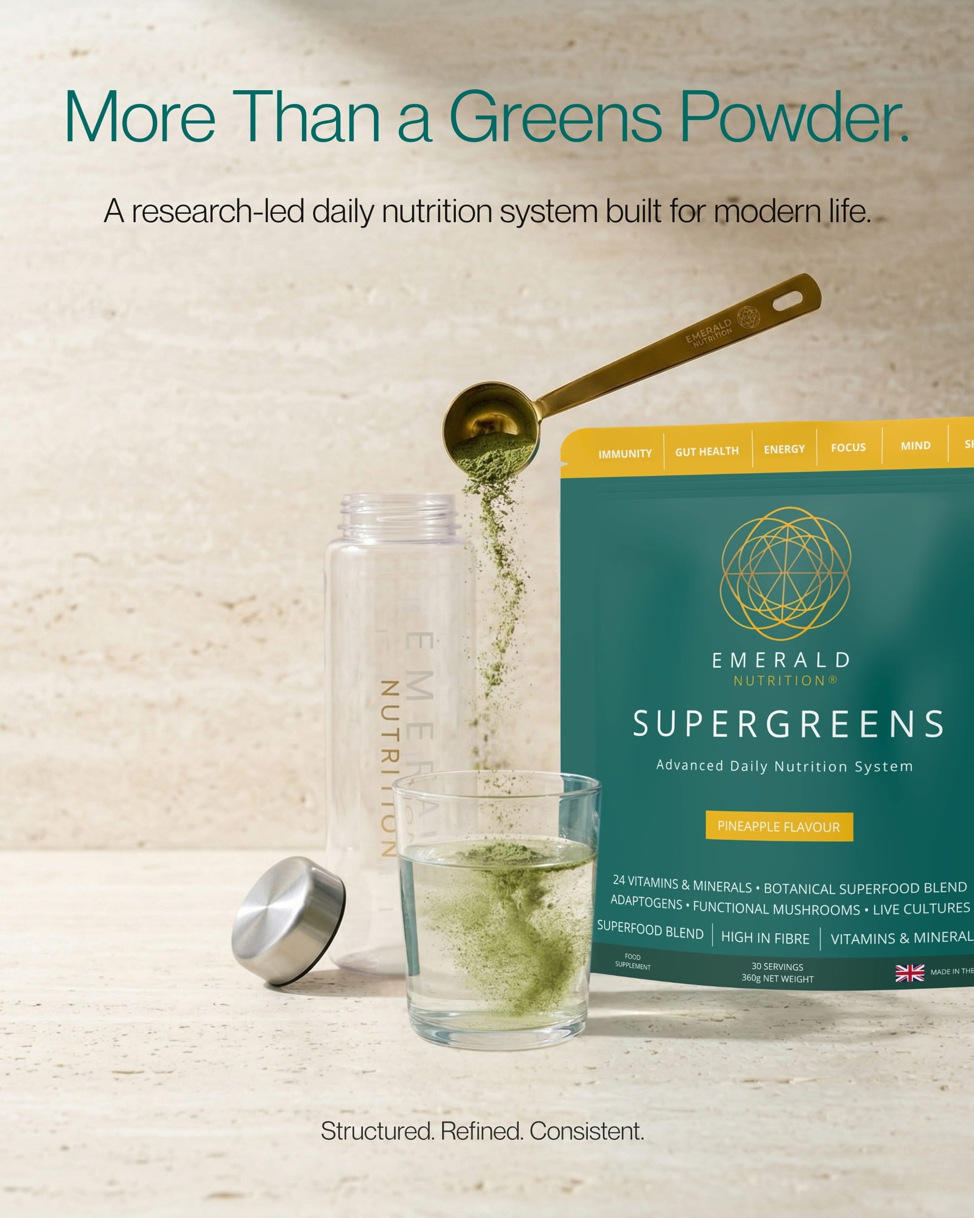 Emerald Nutrition Supergreens packaging with a glass of green liquid and measuring spoon on a light background