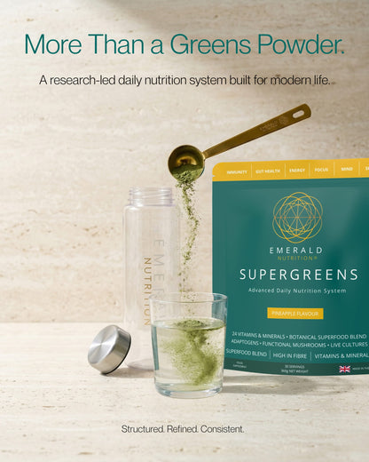 Emerald Nutrition Supergreens packaging with a glass of green liquid and measuring spoon on a light background