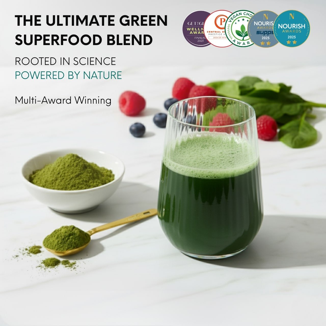 Green superfood blend with a glass of juice, bowl of matcha powder, and fresh berries on a white background.